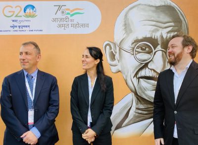 One woman and two men standing in front of conference banner looking to their right